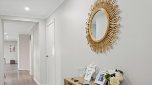 A hallway with a sunburst mirror, a wooden console table with a picture frame, and a small plant. - Spacious Cowes Retreat with BBQ & Boat Parking (Cowes)