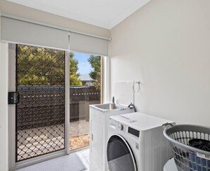Laundry room with washer and dryer, sink, and laundry basket, offering convenient access to the backyard.