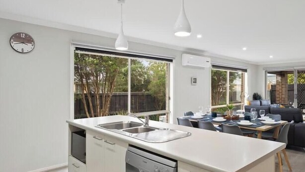 A modern kitchen with a dishwasher, double sink, and a dining area with a table and chairs. - Spacious Cowes Retreat with BBQ & Boat Parking (Cowes)