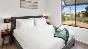 A bedroom with a bed, a ceiling fan, a window with a view of houses, and a painting on the wall. - Getaway for six Accessible accommodation (San Remo)