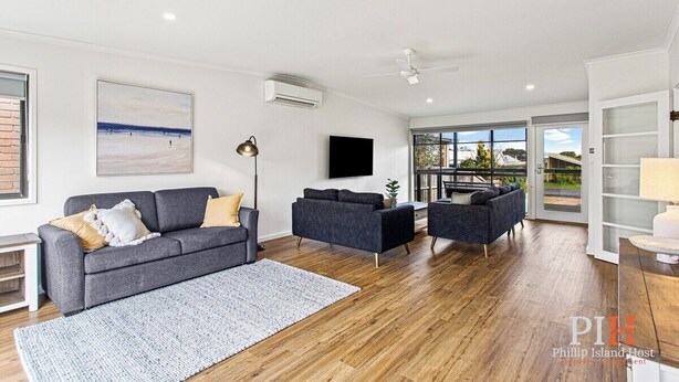 A spacious living room with a grey sofa, a blue armchair, and a large window offering a view of the outdoors. - Getaway for six Accessible accommodation (San Remo)