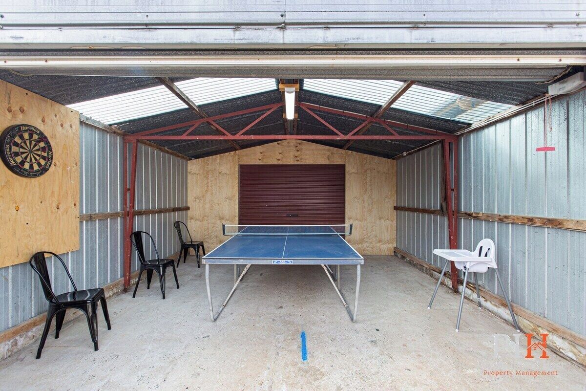 A ping pong table in a covered area with chairs and a dartboard.