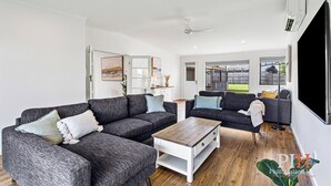 A modern living room with grey sofas, a wooden coffee table, and a large window offering a view of the outdoors. - Getaway for six Accessible accommodation (San Remo)