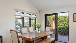 Ein Essbereich mit einem Holztisch, sechs Stühlen, einer Vase mit gelben Blumen und Blick auf einen Garten durch eine Glastür.