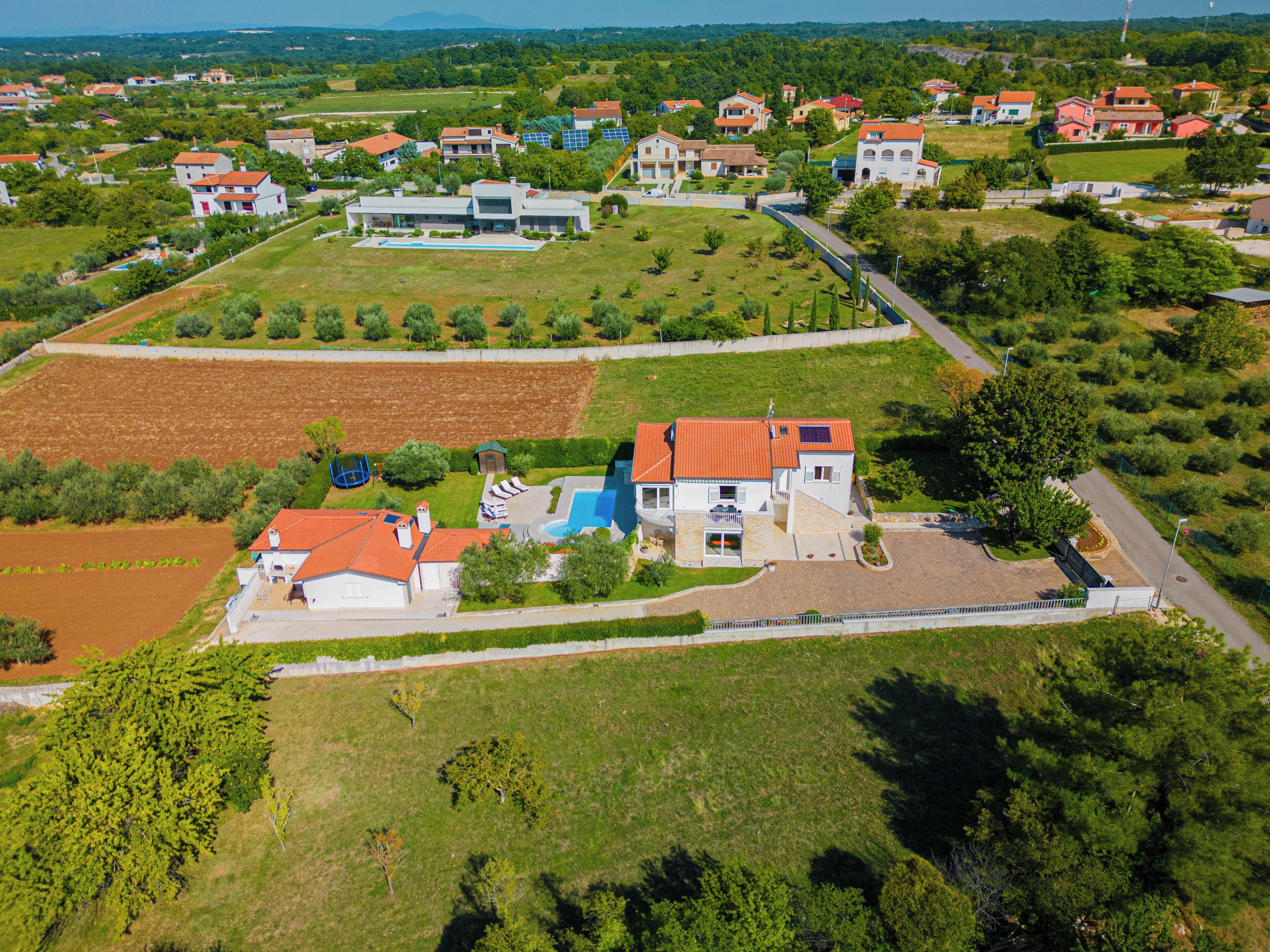 An aerial view of a residential area with houses, a swimming pool, and green fields.