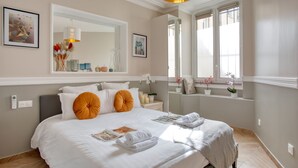 Un dormitorio ordenado con una cama grande, un espejo y una ventana con vistas.