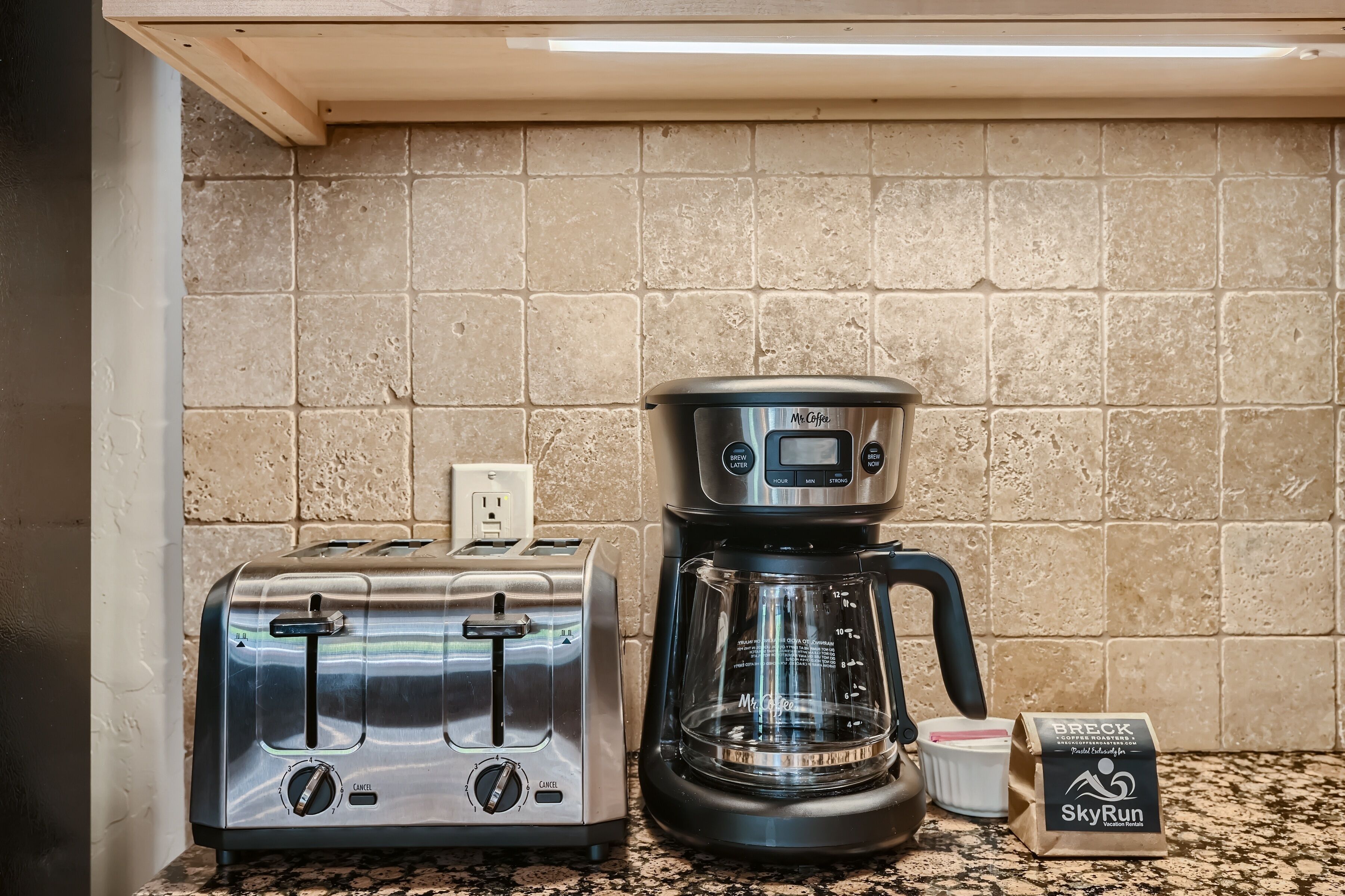Un comptoir de cuisine avec un grille-pain et une machine à café, un paquet de café et un mur en briques.