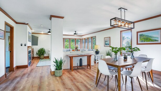A spacious living area with a wooden dining table, white chairs, and a kitchen in the background. - Liho Kai 4 Bedroom Home by RedAwning (Princeville)