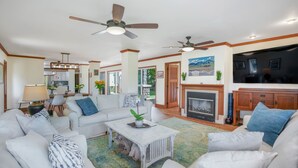 A spacious living room with a fireplace, ceiling fans, and a view of the backyard. - Liho Kai 4 Bedroom Home by RedAwning (Princeville)