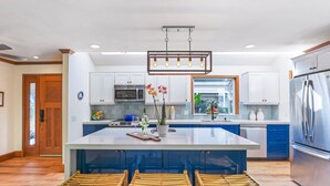 A modern kitchen with a large island, white cabinets, stainless steel appliances, and a wooden dining area. - Liho Kai 4 Bedroom Home by RedAwning (Princeville)