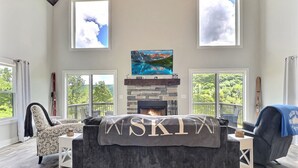 A cozy living room with a fireplace, a sofa, and a TV mounted on the wall. - New Build • Ellicottville Ski Chalet • Sleeps 8 (Ellicottville)