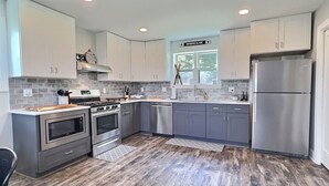 A modern kitchen with stainless steel appliances, grey cabinets, and a wooden floor. - New Build • Ellicottville Ski Chalet • Sleeps 8 (Ellicottville)