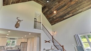 A spacious interior with a high ceiling, wooden beams, a staircase, and a kitchen area. - New Build • Ellicottville Ski Chalet • Sleeps 8 (Ellicottville)