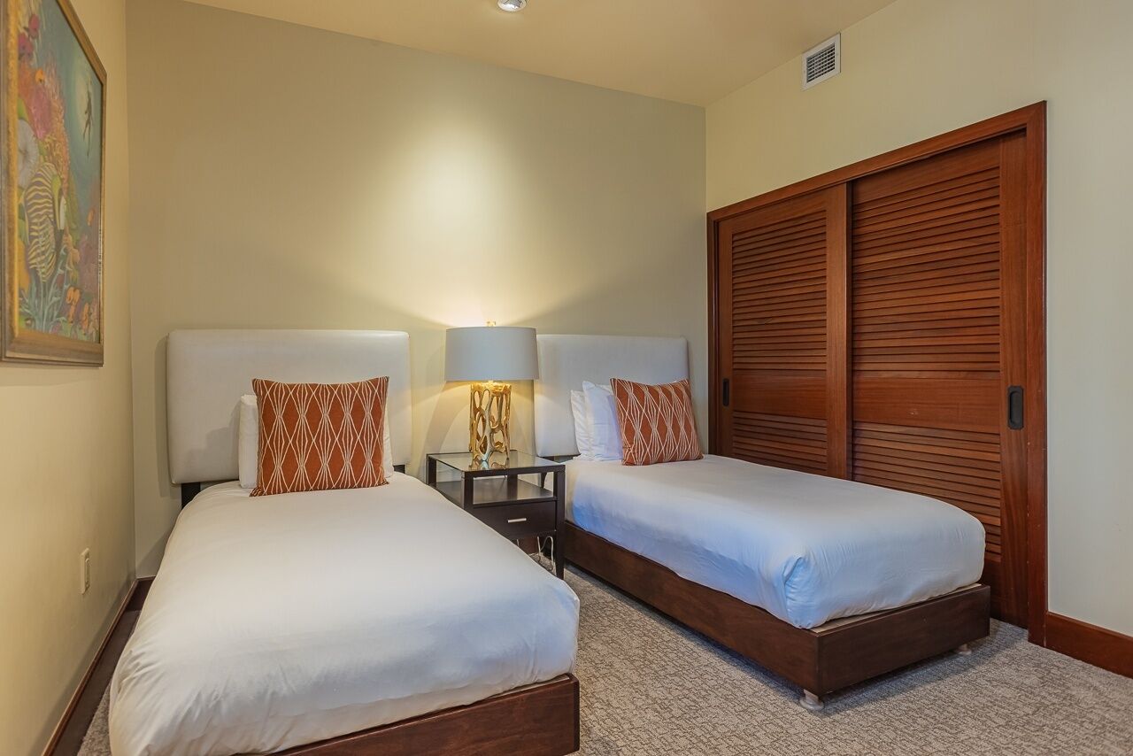 A hotel room with two beds, a nightstand with lamps, and a large wooden closet.