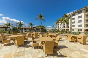 An outdoor patio with wicker furniture and a clear view of a multi-story building in the background. - Wailea Beach Villas M312 3 Bedroom Condo (Kihei)