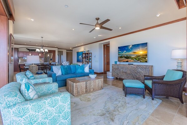A spacious living area with a blue sofa, a wooden coffee table, and a wicker chair. - Wailea Beach Villas M312 3 Bedroom Condo (Kihei)