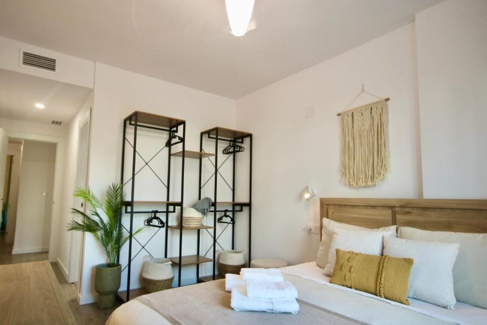 A modern hotel room with a bed, bedside table, and a wall-mounted shelf unit.
