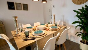 Mesa de jantar posta com pratos, copos e talheres, rodeada por cadeiras brancas.