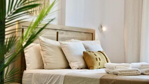 Cama bem arrumada com lençóis brancos, cabeceira de madeira e uma única almofada decorativa.