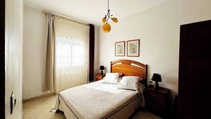 A bedroom with a bed, two bedside tables, a wooden headboard, a window with curtains, and two framed pictures on the wall. - Center city Clean Family Appartement (Tétouan)