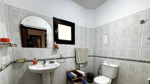 A bathroom with a pedestal sink, a toilet, and a mirror. There is a towel rack with towels and a basket. - Center city Clean Family Appartement (Tétouan)