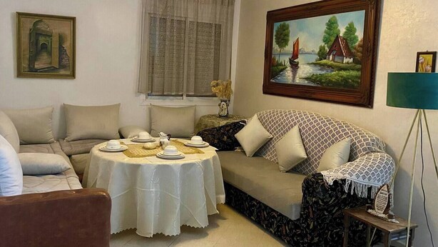 A cozy living room with a round table set for dining, a sofa, and a painting on the wall. - Center city Clean Family Appartement (Tétouan)