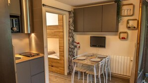 A compact kitchen with a built-in stove, a dining area with a table and chairs, a bed with a wooden headboard, and a TV mounted on the wall. - 5th floor, balcony, tv, ski locker, 20m², Les Orres (Les Orres)