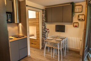 A compact kitchen with a built-in stove, a dining area with a table and chairs, a bed with a wooden headboard, and a TV mounted on the wall. - 5th floor, balcony, tv, ski locker, 20m², Les Orres (Les Orres)