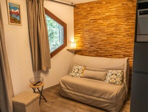A compact room with a sofa, a small table, a window with curtains, and a wall with a wooden pattern. - 5th floor, balcony, tv, ski locker, 20m², Les Orres (Les Orres)