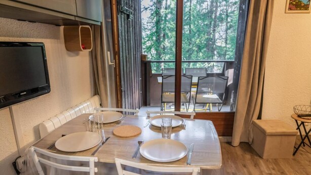A dining area with a table set for two, chairs, a television mounted on the wall, and a view of the outdoors through a large window. - 5th floor, balcony, tv, ski locker, 20m², Les Orres (Les Orres)