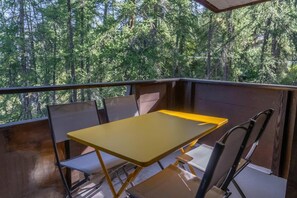 A balcony with a yellow table and chairs, overlooking a dense forest. - 5th floor, balcony, tv, ski locker, 20m², Les Orres (Les Orres)