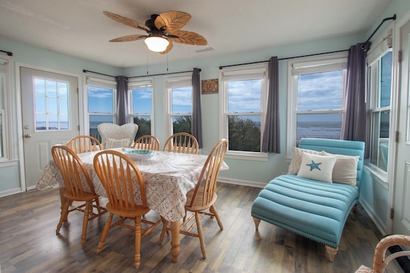 A dining area with a table and chairs, a ceiling fan, and large windows with curtains.