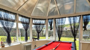 A pool table in a conservatory with large windows and a view of a garden. - Nicely Tucked Away Cottage (Millbrook)