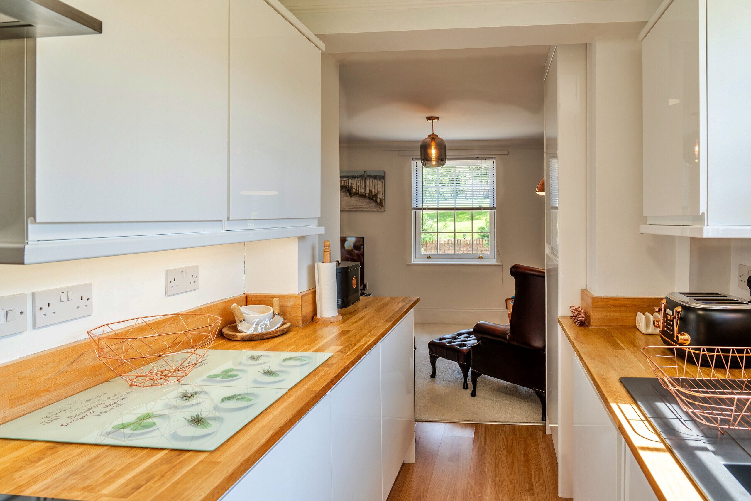 A modern kitchen with white cabinets, a wooden countertop, and a view to a dining area.