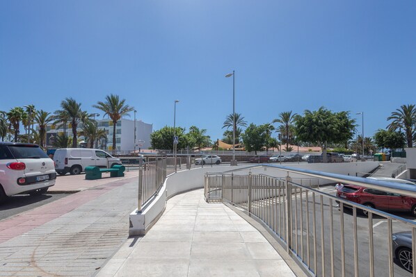 A parking area with a curved walkway, palm trees, and a building in the background. - Complejo Aloe - Pool - close to Maspalomas Beach (San Bartolomé de Tirajana)