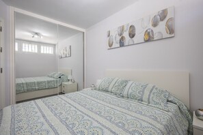 A bedroom with a bed, a nightstand, a mirror, and a wall with abstract art. - Complejo Aloe - Pool - close to Maspalomas Beach (San Bartolomé de Tirajana)