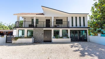 Une maison moderne à deux étages, dotée d’un balcon, de grandes fenêtres et d’une allée gravillonnée.