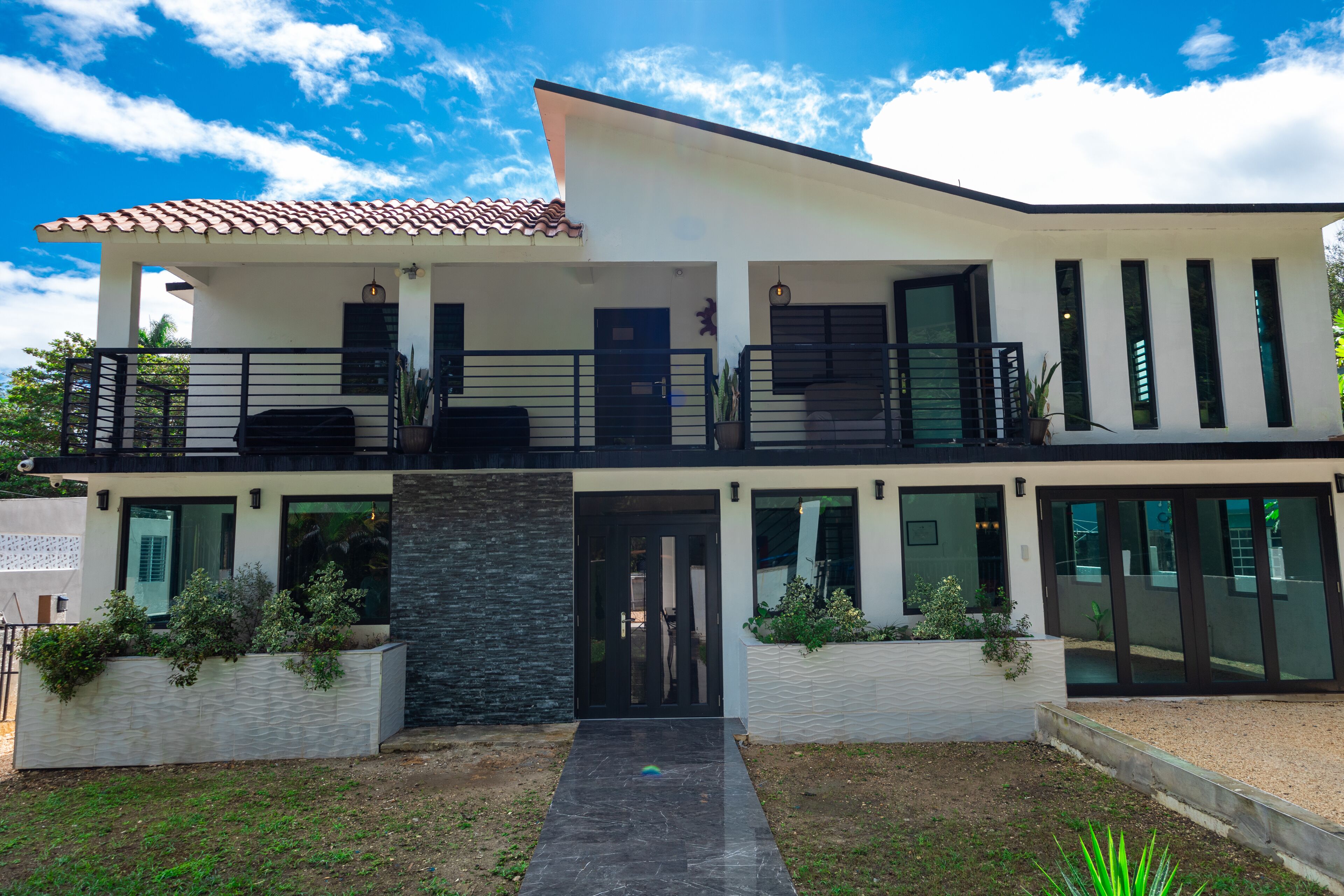 Une maison moderne à deux étages, dotée d’un balcon, de grandes fenêtres et d’une façade en pierre.
