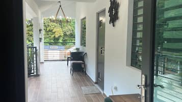 Un hall d’entrée spacieux, doté d’un parquet en bois, d’un lustre et offrant une vue sur un balcon agrémenté de verdure.