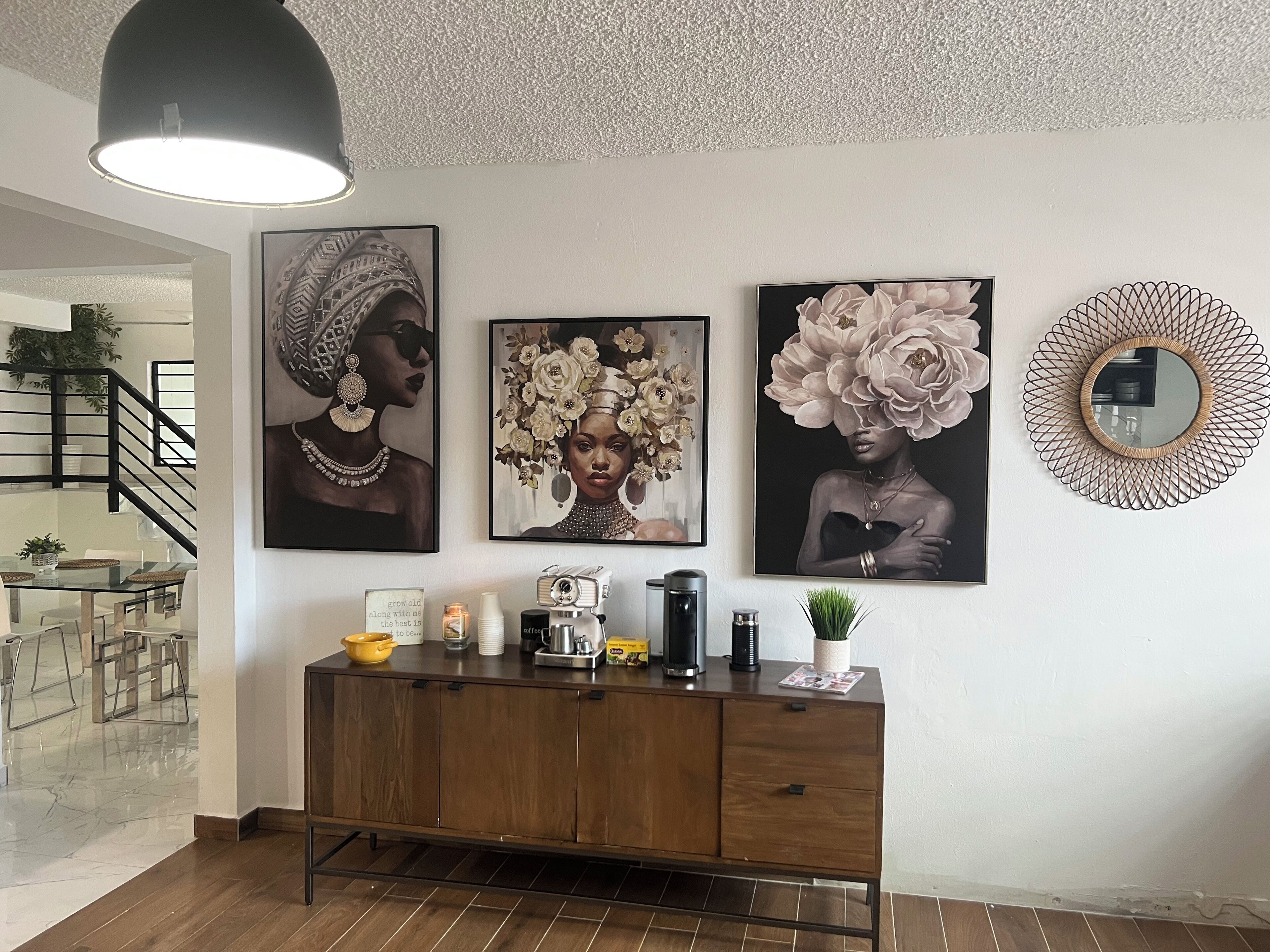 Un salon moderne avec un meuble en bois, un luminaire suspendu noir et trois œuvres d’art encadrées accrochées au mur.