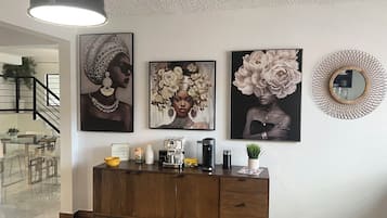 Un salon moderne avec un meuble en bois, un luminaire suspendu noir et trois œuvres d’art encadrées accrochées au mur.