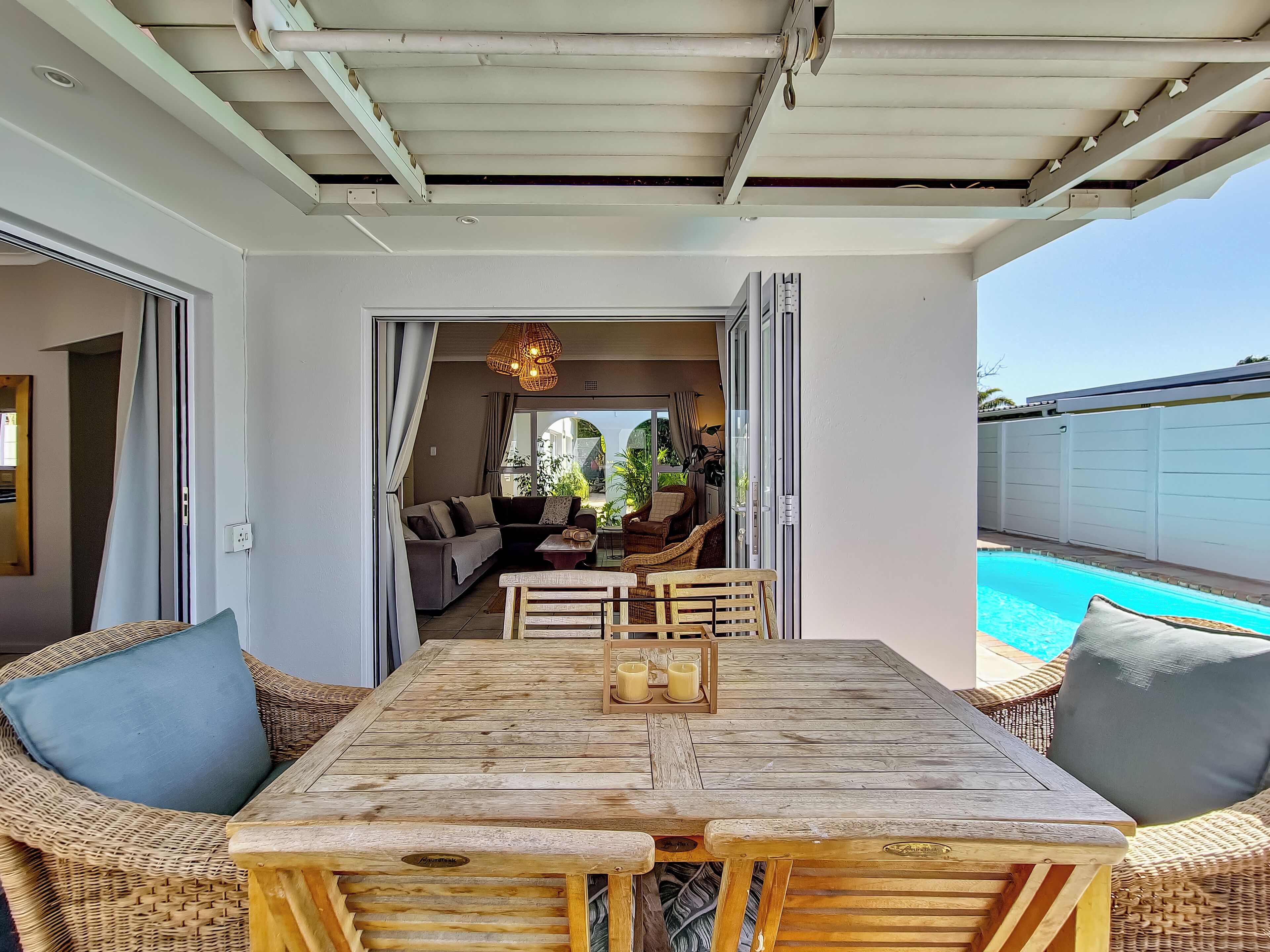 Une table à manger en bois avec des chaises, un canapé et une vue sur une piscine.