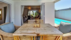 Uma mesa de jantar de madeira com cadeiras, um sofá e vista para uma piscina.