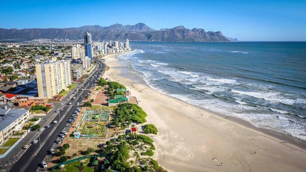 Paisagem costeira com praia, edifícios altos e montanhas ao fundo.