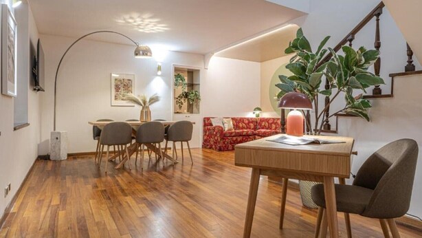 Un salon moderne avec un plancher en bois, un coin repas avec une table et des chaises, un canapé rouge et un escalier.