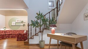Un salon moderne avec un plancher en bois, un canapé à motifs floraux rouges, une table en bois avec une lampe et un escalier agrémenté d’une plante.