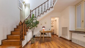 Un escalier en bois mène à une pièce où se trouvent un bureau, une plante en pot et un radiateur.