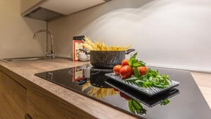 Une cuisine équipée d’une plaque de cuisson à induction, un faitout de spaghettis, des tomates fraîches et du basilic sur le plan de travail.