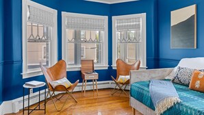 A room with blue walls, three windows with white frames, a bed with a blue and white bedspread, and two leather chairs. - Updated, Historic District, Walk to Waterfront. Pet-Friendly! Sleeps 12 (Warren)