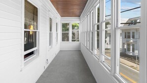 A narrow corridor with white walls and large windows on one side, leading to a covered area with a wooden ceiling. - Updated, Historic District, Walk to Waterfront. Pet-Friendly! Sleeps 12 (Warren)